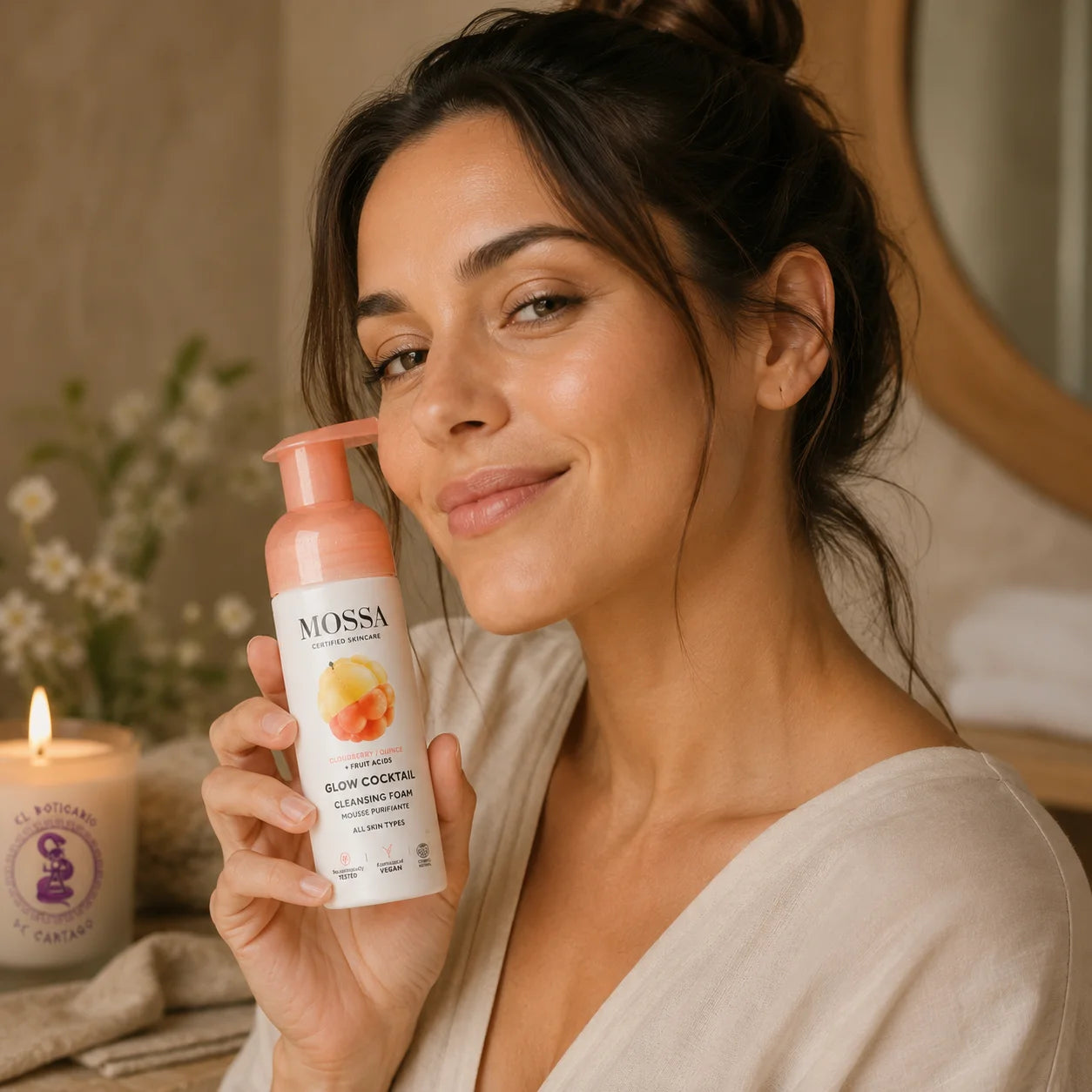 Modelo sosteniendo la espuma limpiadora facial MOSSA Glow Cocktail en un ambiente spa premium con vela decorativa de El Boticario de Cartago.